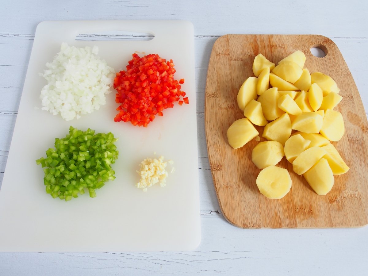 Pelamos y cortamos las patatas chascándolas. Picamos muy fino el ajo y la cebolla y cortamos en cuad