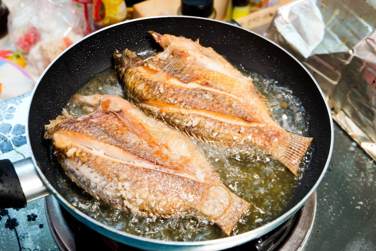 Pescado friéndose en una sartén con mucho aceite