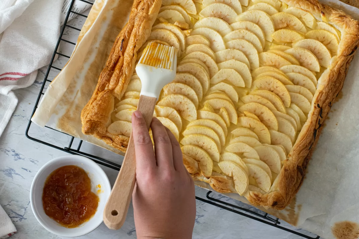 Pincelamos con mermelada la tarta de manzana y hojaldre con crema pastelera