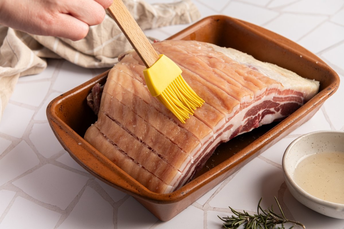 Pintando la piel con vinagre para hacer panceta al horno