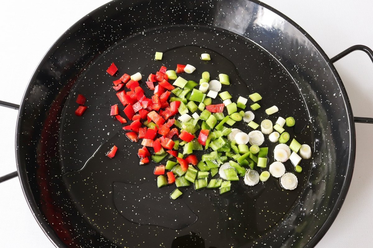 Pochar los ajos tiernos y los pimientos para la paella de verduras
