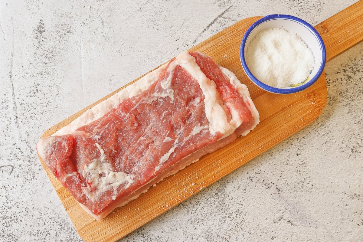 Poner sal a la panceta para hacer los chicharrones de Cádiz