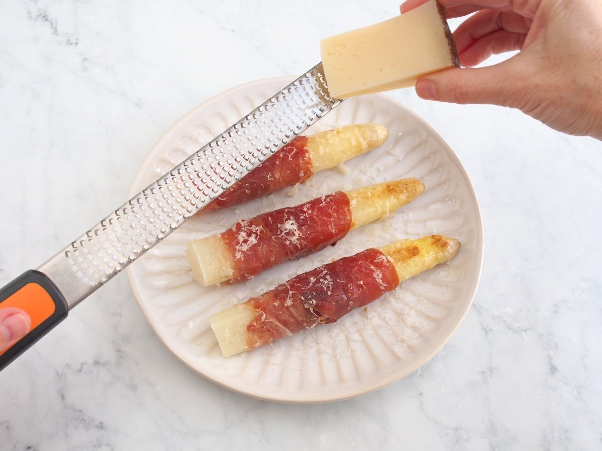 Rallar queso por encima de los espárragos blancos con jamón
