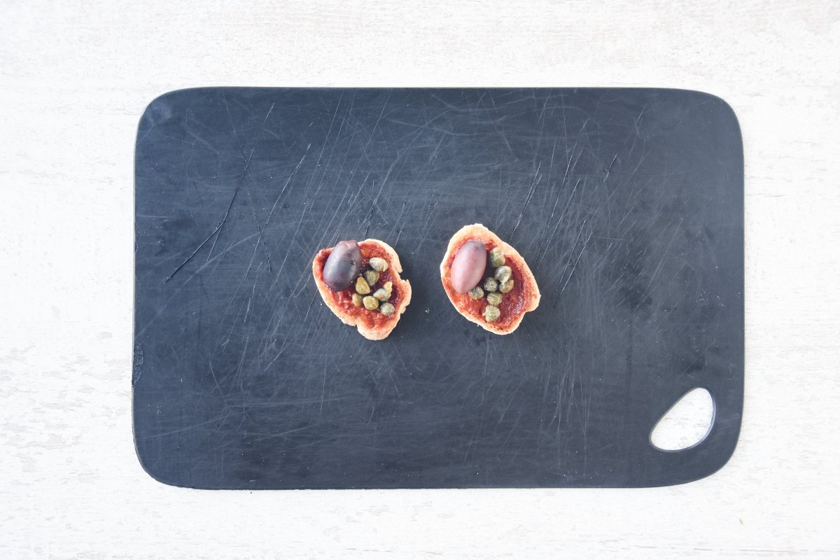 Repartimos el tapenade y cubrimos con aceitunas y alcaparras