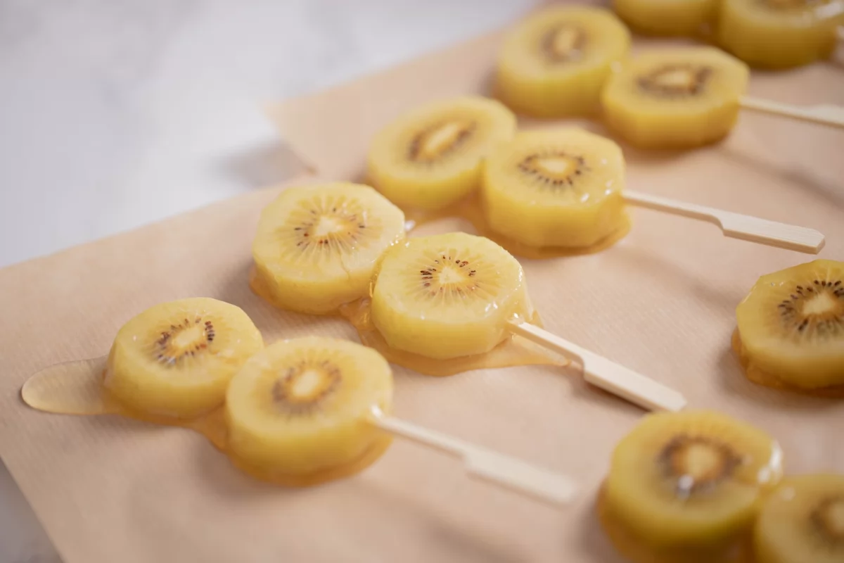 Rodajas de kiwi amarillo en brochetas sobre papel vegetal