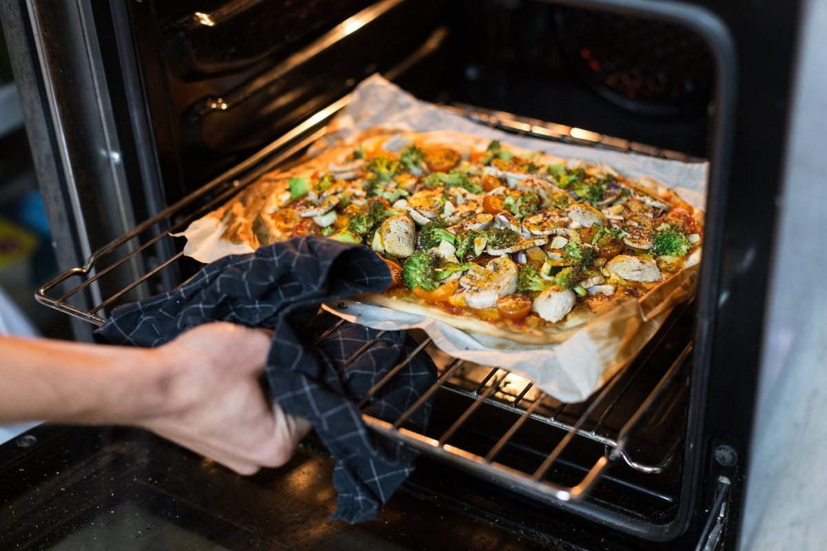 Sacando del horno una pizza casera de verduras recién hecha