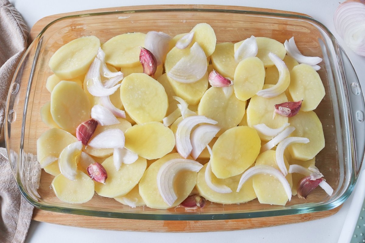 Salpimentar y añadir cebolla y ajo a las patatas para el pollo asado al horno con patatas