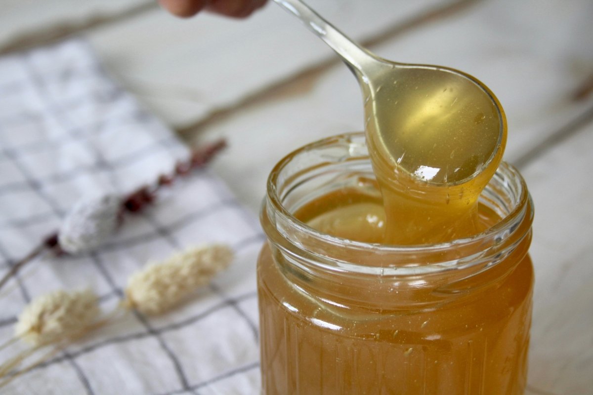 Tarro de vidrio con miel y una cuchara de metal recién sacada de su interior con miel