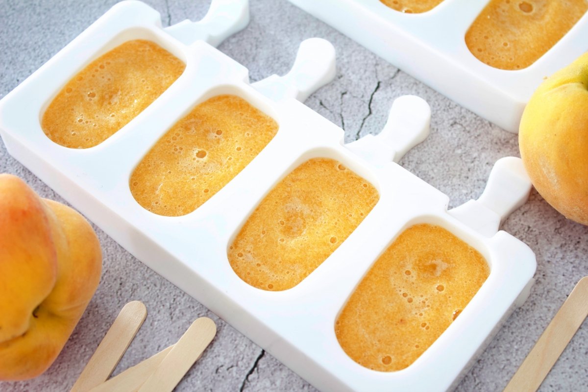 Crushing peaches and putting it in the molds to continue making the peach popsicles