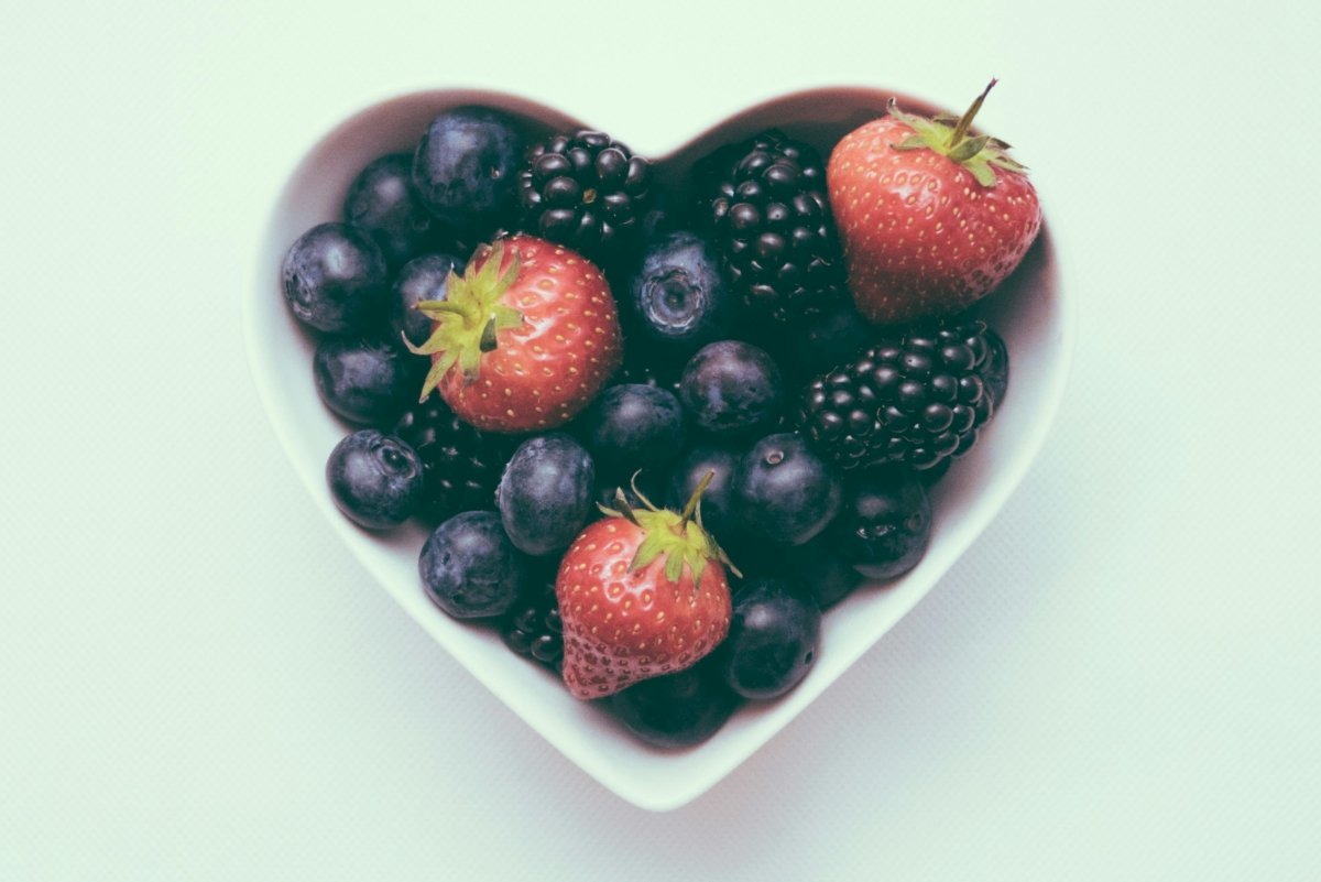 Un cuenco con forma de corazón con fresas y frutas rojas afrodisiacas