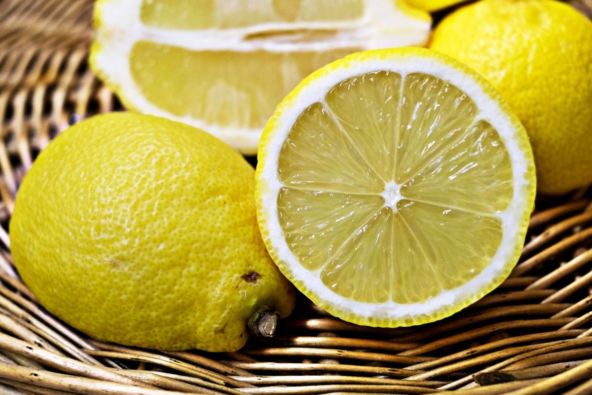 Un frutero de mimbre con varios limones, en primer plano uno entero y la mitad de otro