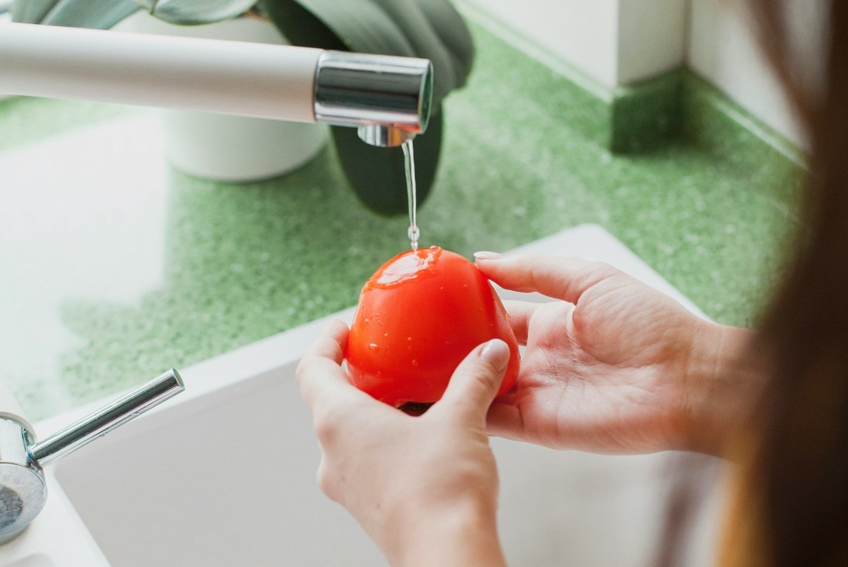 Un tomate debajo del grifo de agua para ser limpiado