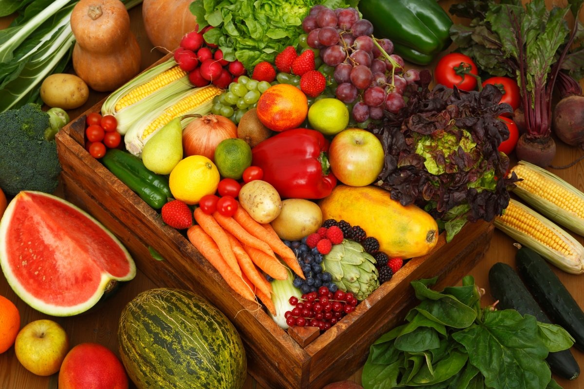 Una caja llena de frutas y verduras con limones, frutos rojos, sandía, melón...