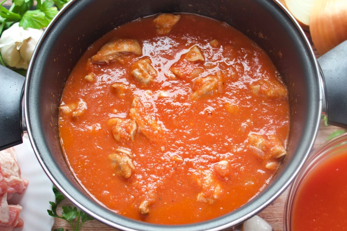 Una olla con el cordero y el tomate triturado para hacer el cordero en salsa de tomate