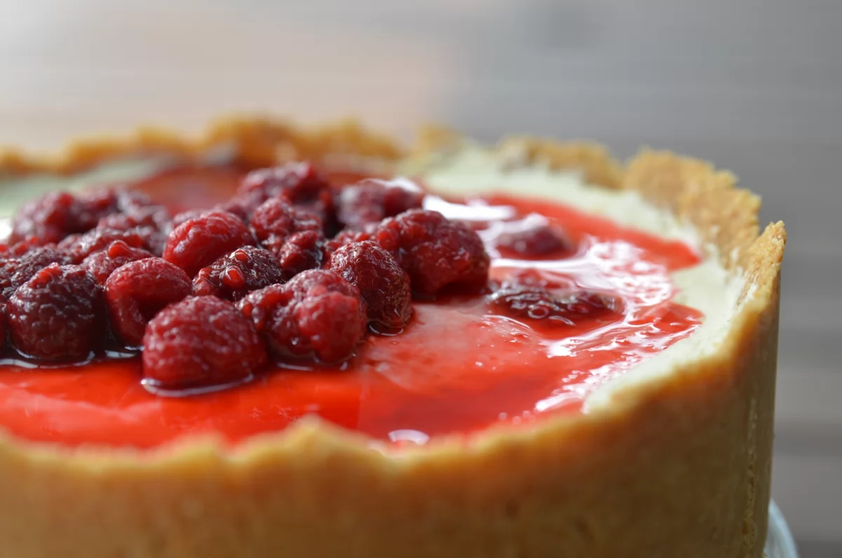 Una tarta de queso cubierta con mermelada de frambuesas y frambuesas enteras por encima