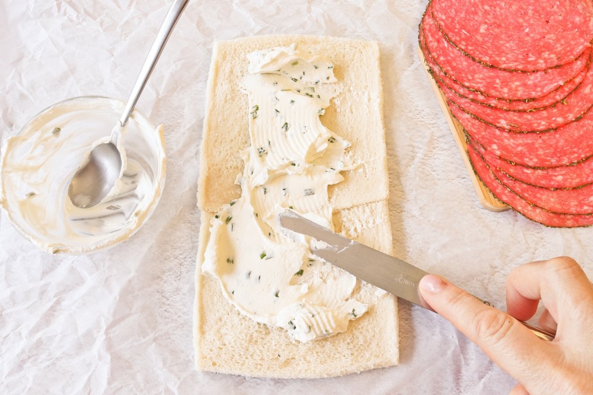 Untar con queso crema el primer rollo de pan de molde