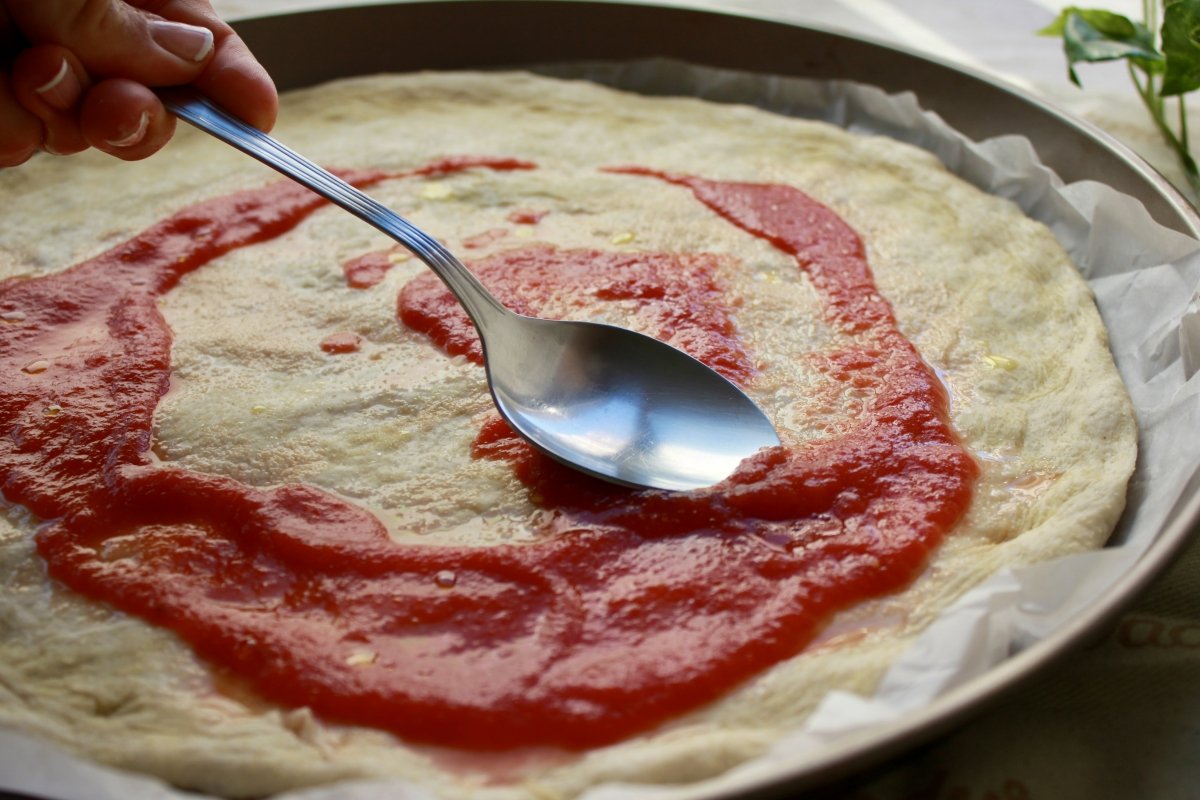 Vista de la salsa de tomate extendida sobre la masa de pizza