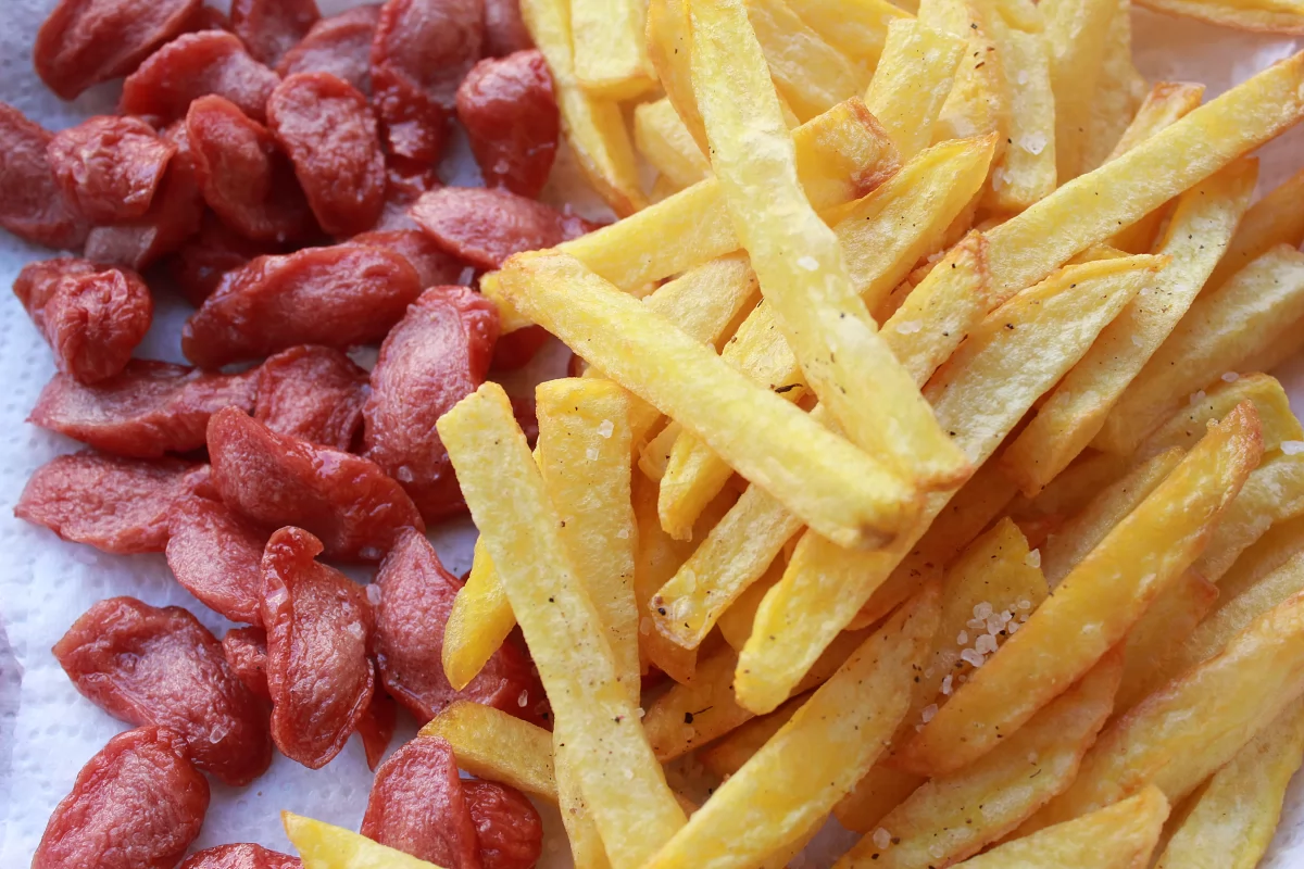 Vista de las patatas y las salchichas fritas sobre papel absorbente *